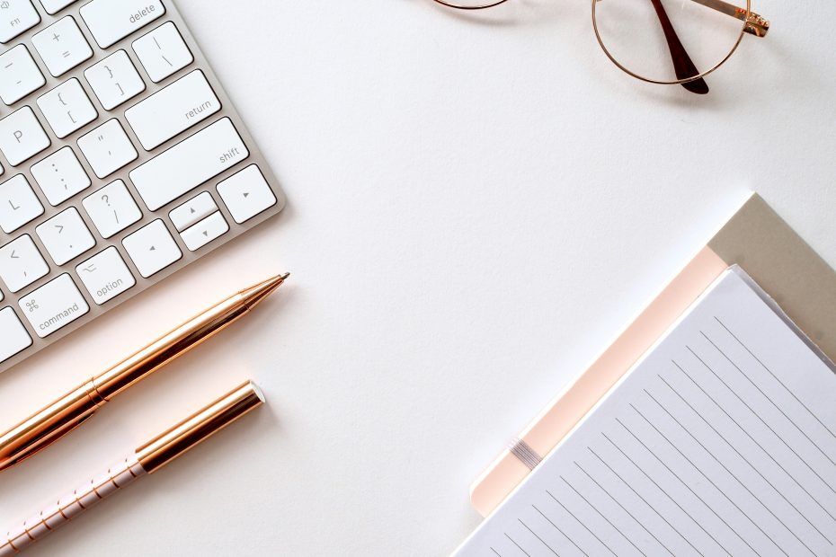 a keyboard, glasses, pen and notepad on a desk